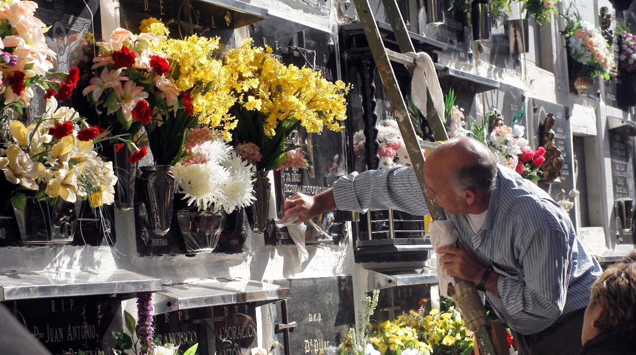 Un hombre adecenta una lápida en el cementerio