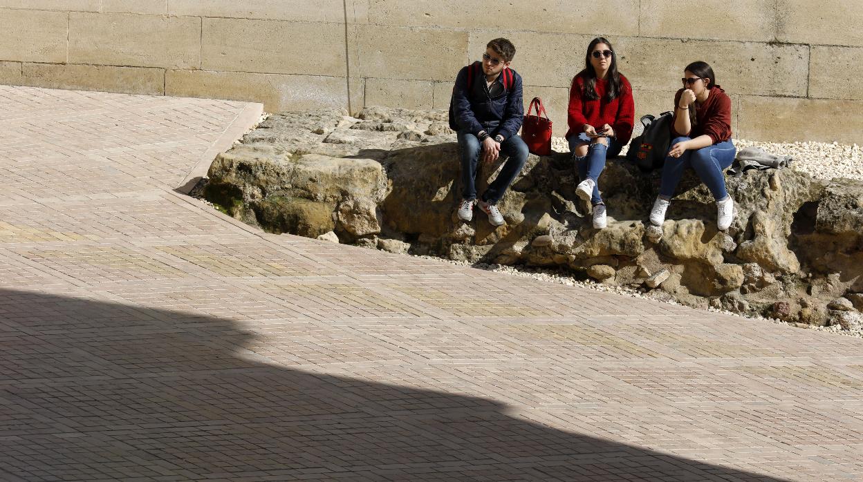 Tres jóvenes descansan al sol junto a la Puerta del Puente