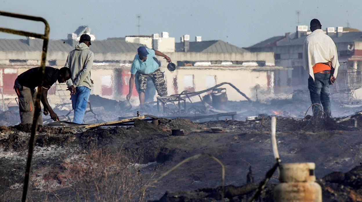 Inmigrantes recogen restos de sus chabolas tras un incendio en un poblado