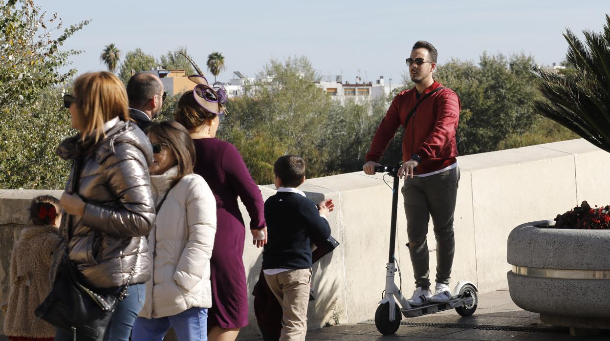 Un joven circula con un patinete eléctrico por el Puente Romano de Córdoba