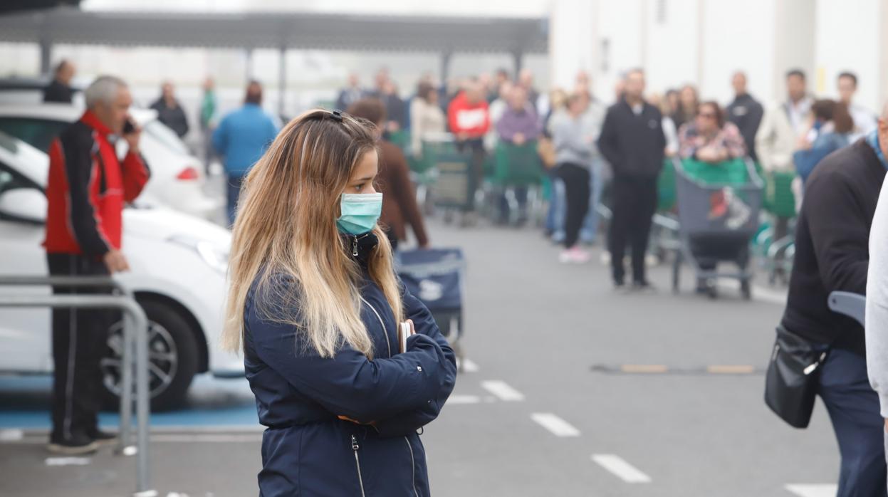 Una joven con mascarilla espera a la apertura de un supermercado de la capital