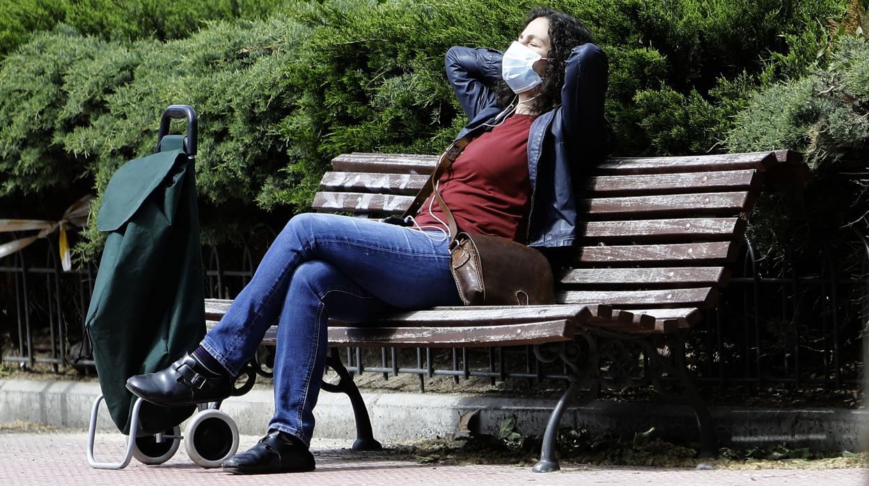 Una mujer descansa al sol sentada en un banco durante el estado de alarma