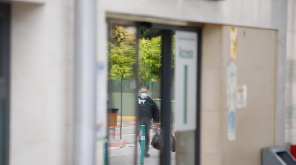 Una persona con mascarilla reflejada en una puerta del Hospital Reina Sofía