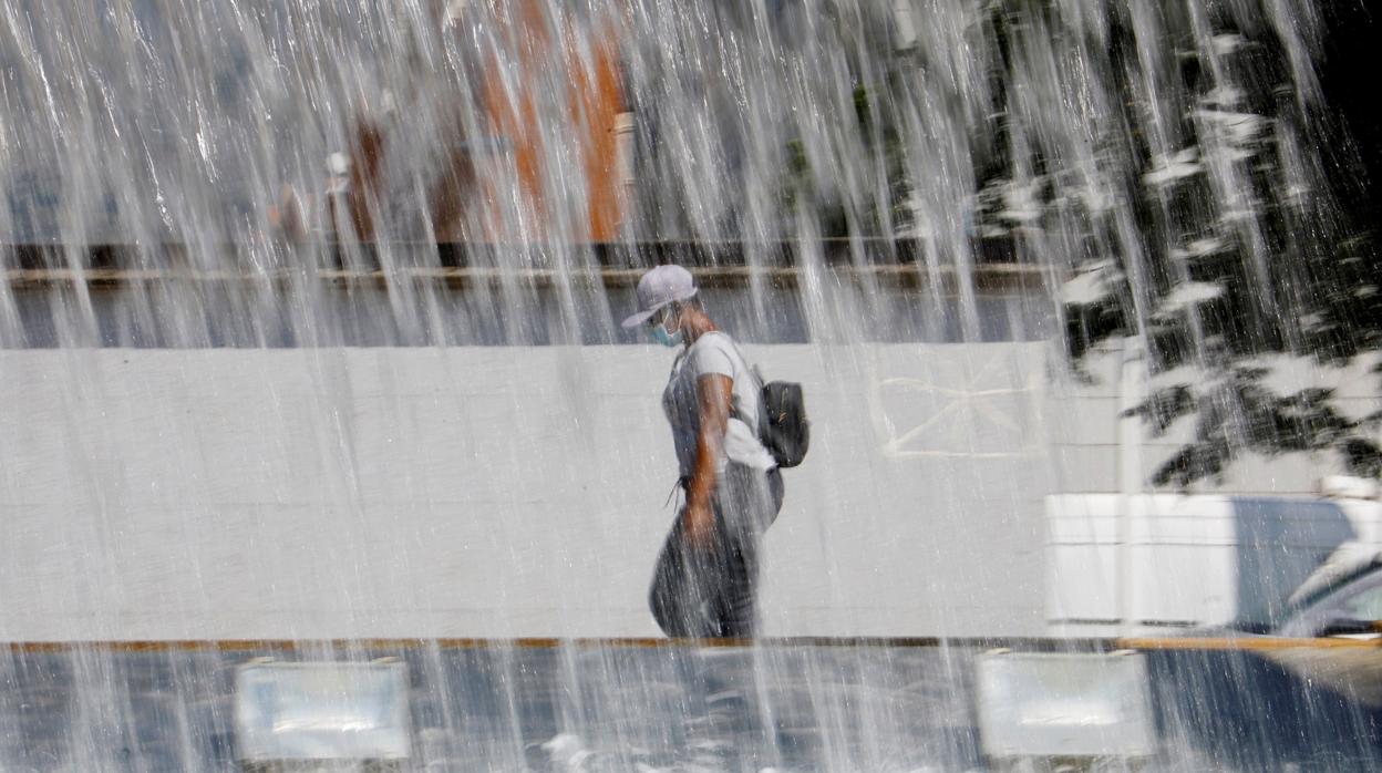 Una joven ataviada con gorra y mascarilla pasea junto a una de las fuentes del Vial de Córdoba