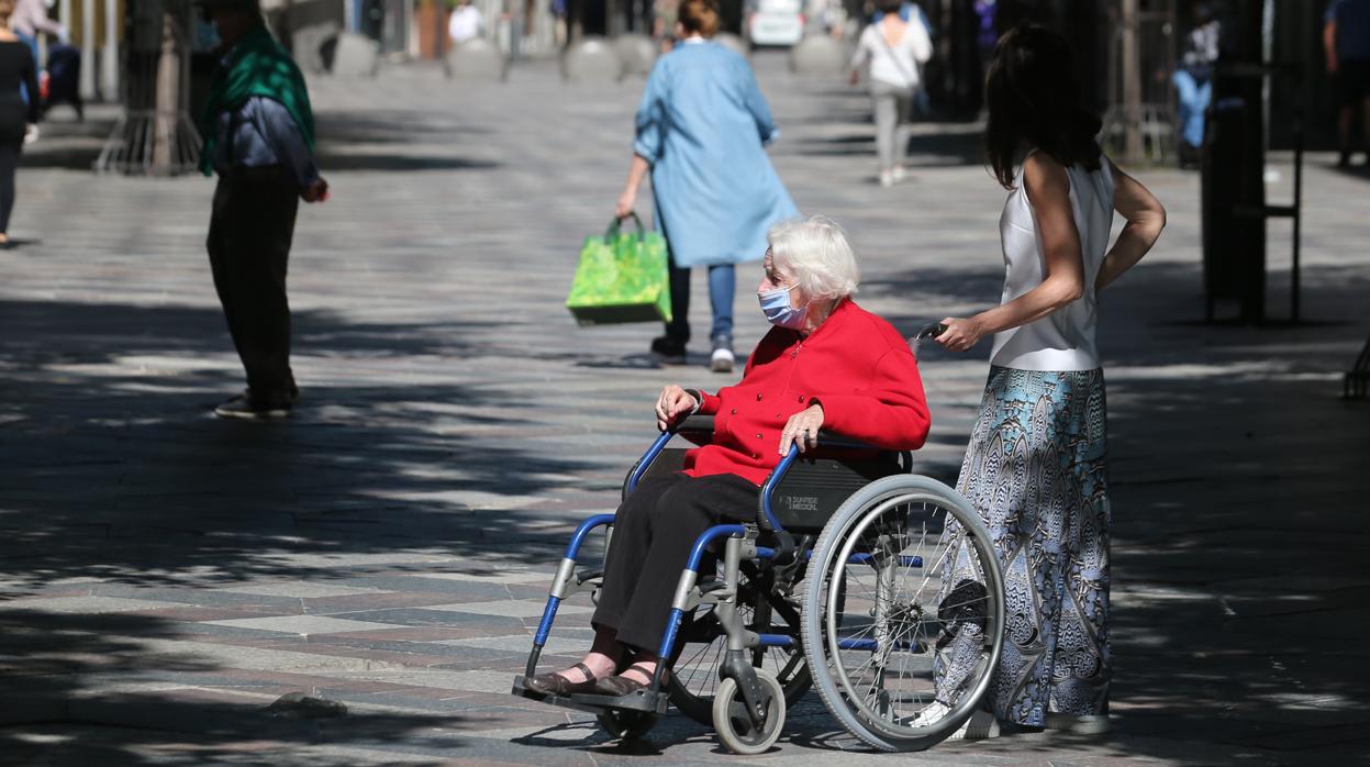 Una mujer en silla de ruedas con mascarilla es ayudada por una joven