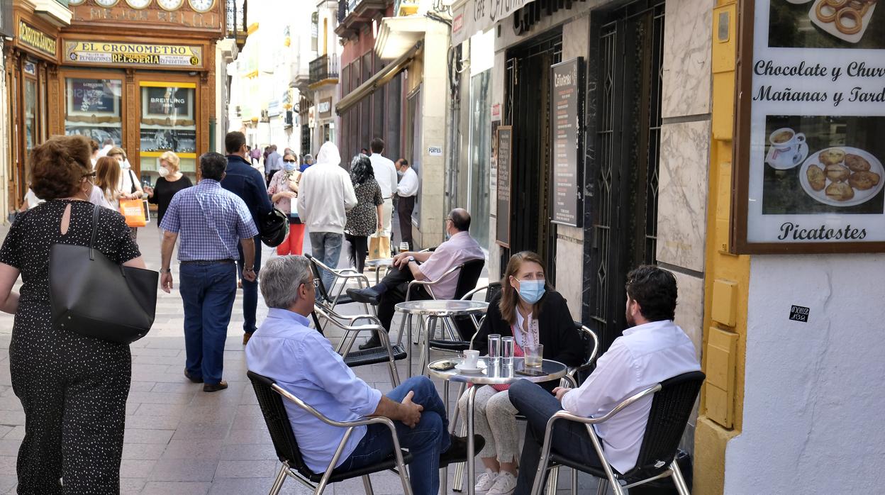 Varias personas, ataviadas con mascarillas, conversan en la puerta de un bar de Sevilla