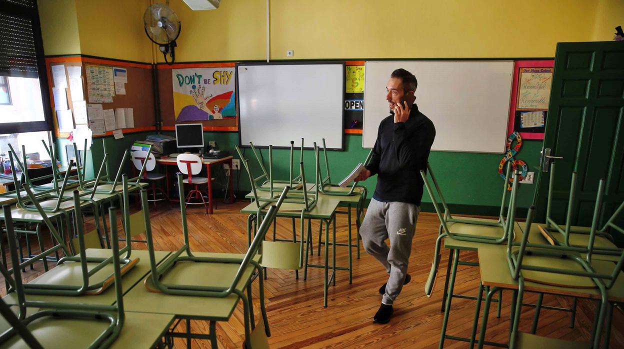 Un docente habla por su teléfono móvil en un aula desierta en el colegio público