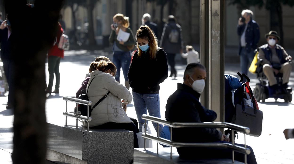 Varias personas al sol otoñal en el bulevar de Gran Capitán