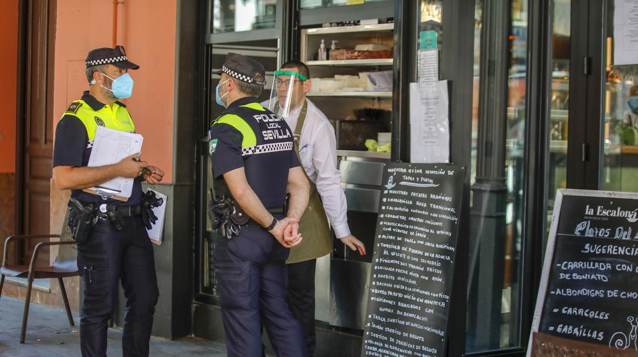 Los veladores en la capital sevillana van a reducir su aforo a la mitad. En la imagen, la Policía Local de Sevilla comrpueba las medidas de un bar