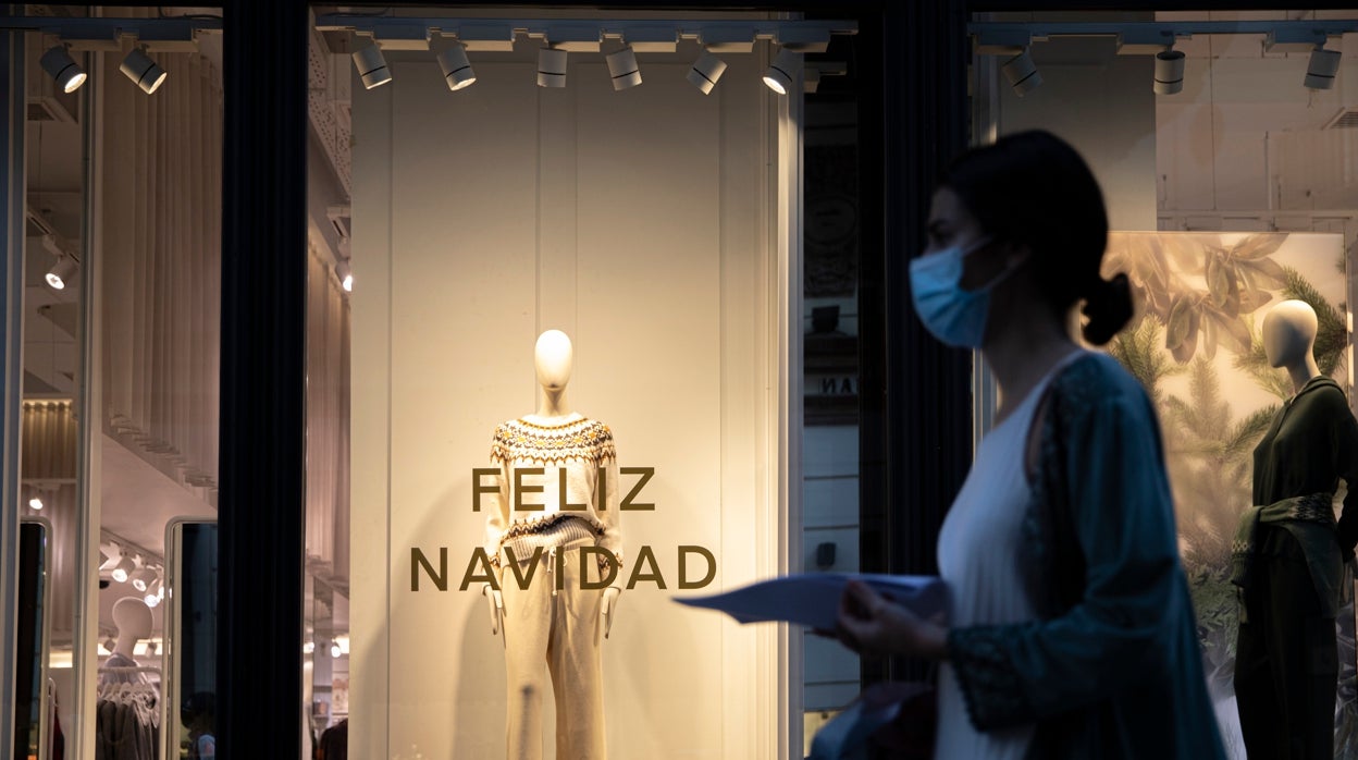 Una joven con mascarilla pasa ante un comercio con mensajes navideños en Sevilla