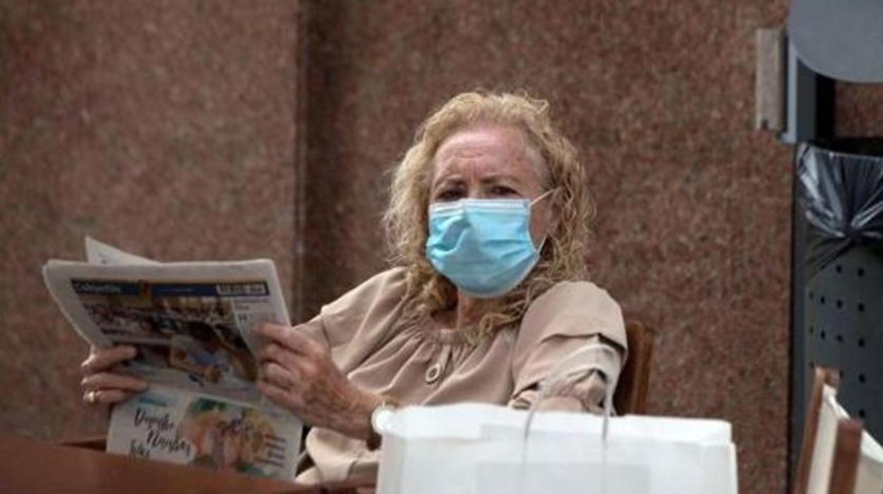 Una mujer lee el periódico con la mascarilla puesta