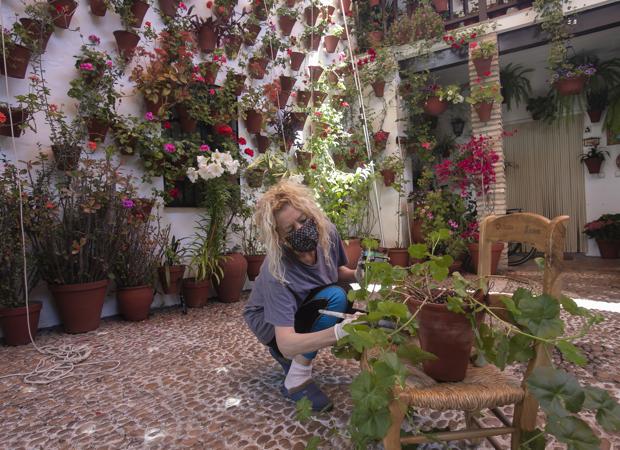 Una mujer pinta una maceta sobre una silla de enea en un patio de la calle Martín de Roa de Córdoba