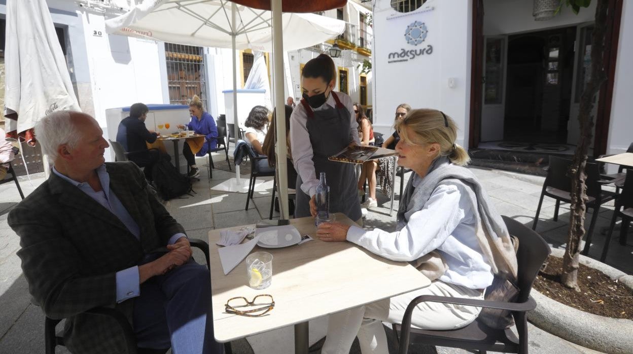 Una camarera atiende a dos clientes en la terraza de Macsura Gastrotaberna