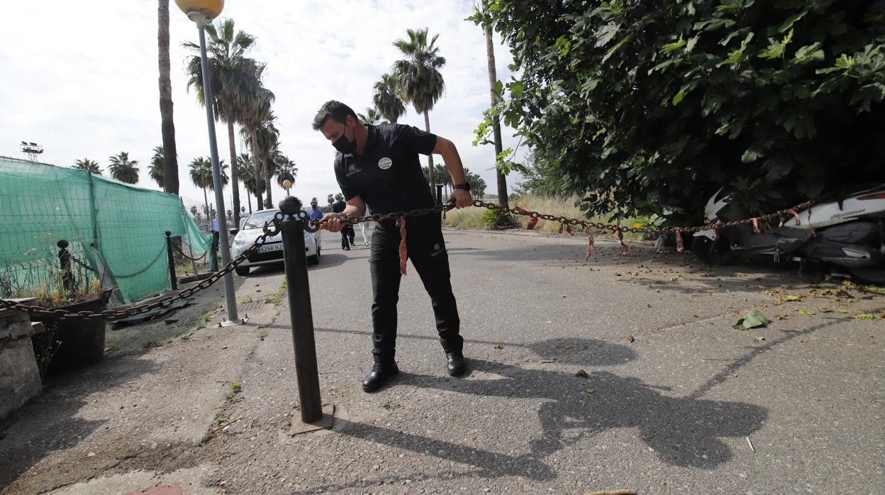 Un vigilante de seguridad coloca una cadena para cerrar el paso a los campos de la Ciudad Deportiva