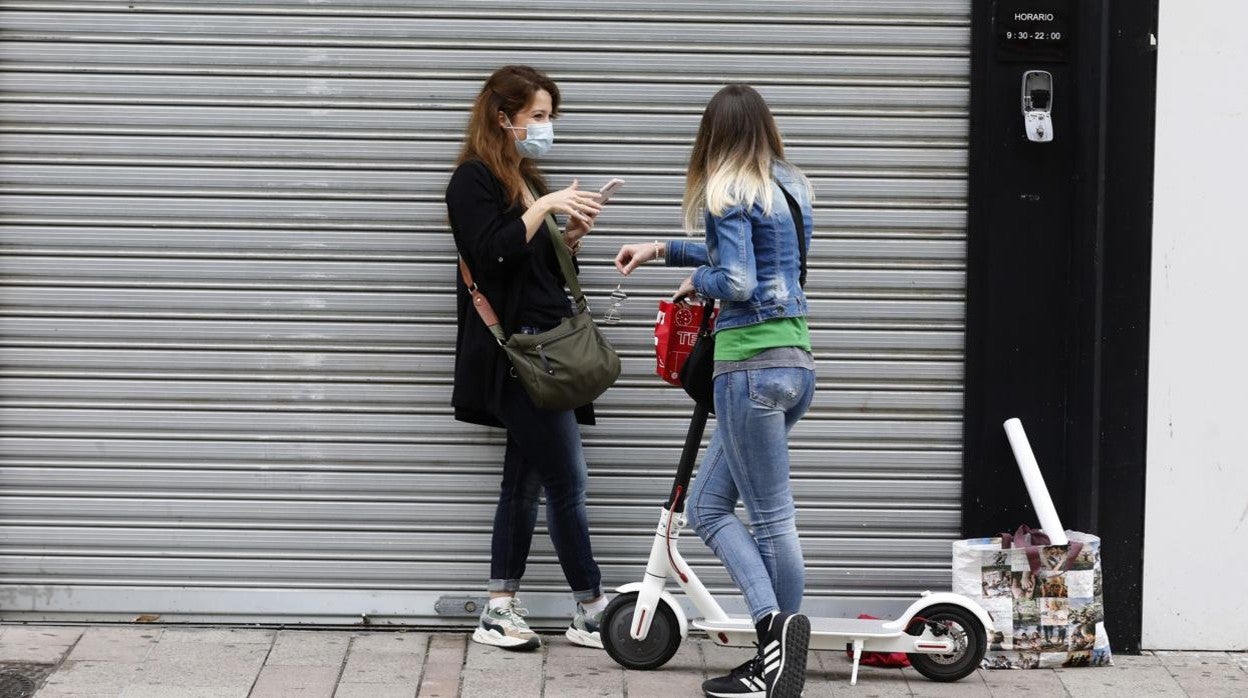 Dos jóvenes, en una de las fases de la desescalada con la mascarilla junto a un escaparate