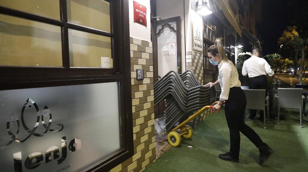 Una camarera introduce un bloque de sillas en el interior de un restaurante de Córdoba