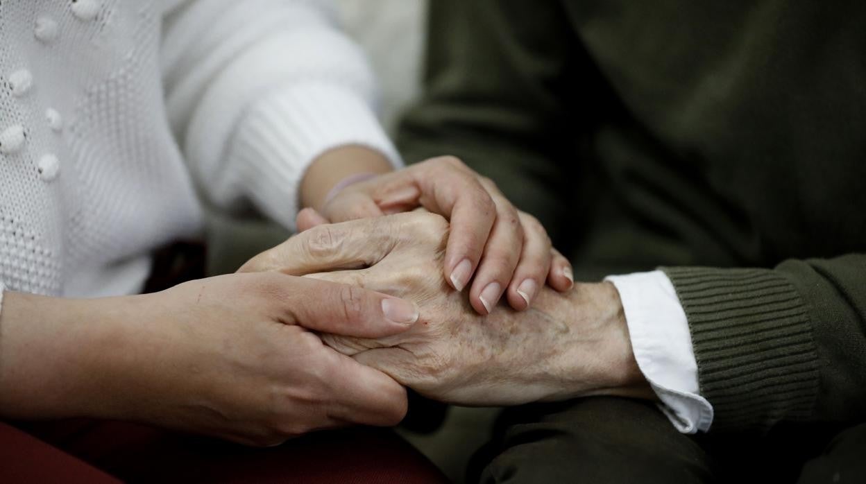 Una cuidadora sostiene la mano de un dependiente