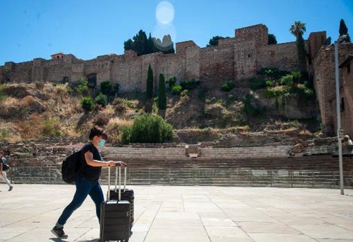 Una turista camina con sus maletas por la calle Alcazabilla, junto al Teatro Romano y la Alcazaba de Málaga