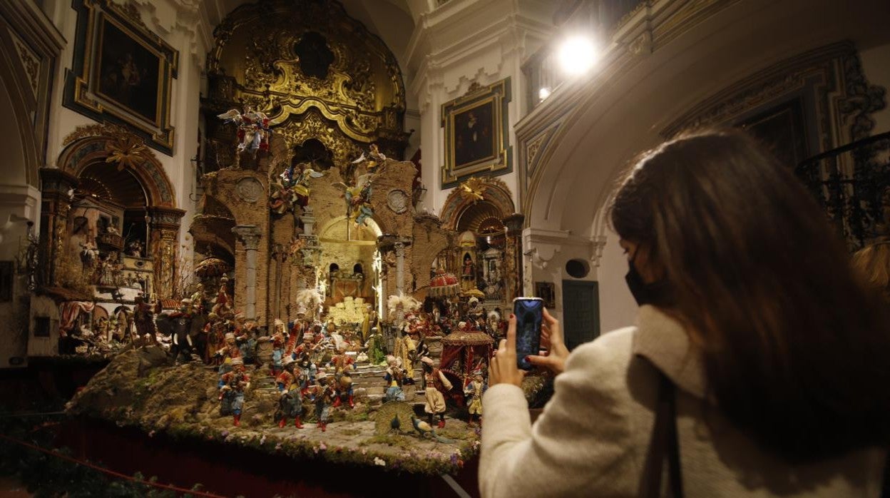 Una chica fotografía el Belén de la Hermandad de la Sentencia, premio al menor nacimiento napolitano