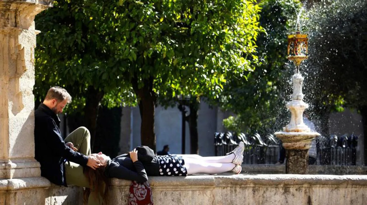 Unos turistas toman el sol en una de las fuentes del patio de los naranjos de la Mezquita - Catedral de Córdoba en una jornada de temperaturas primaverales