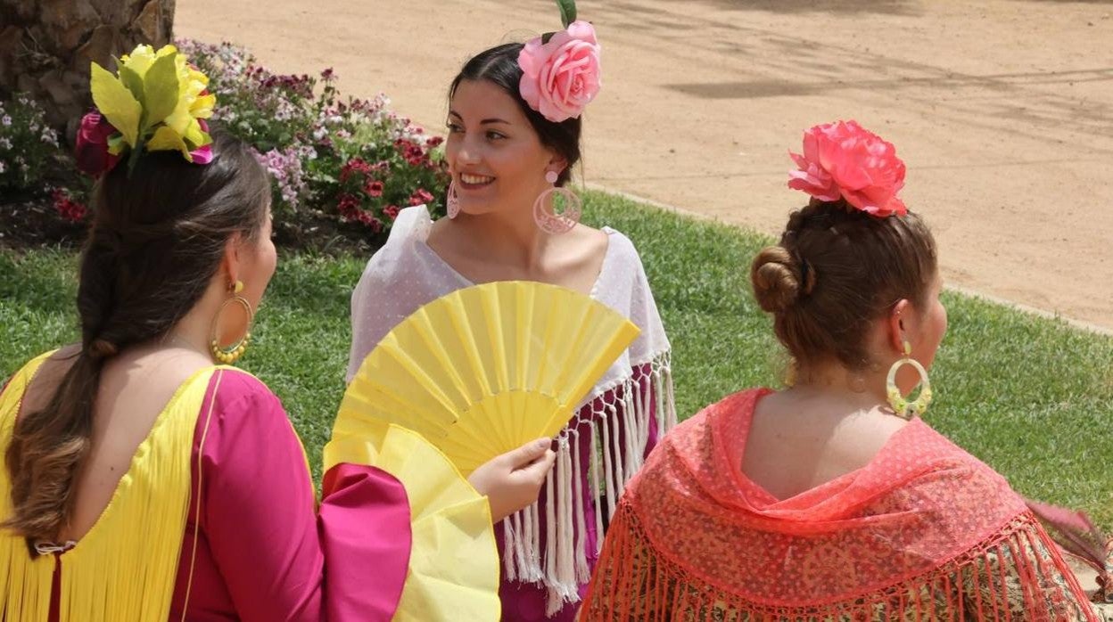 Una joven vestida de flamenca se abanica junto a la portada de la Feria de Córdoba