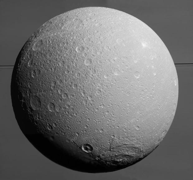Dione con Saturno y sus anillos en el fondo