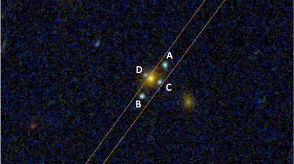 La nueva Cruz de Einstein J2211-3050. Se trata de una galaxia elíptica (objeto amarillo), relativamente cercana, que actúa de lente. Los cuatros objetos azules (ABCD) son las imágenes producidas de una galaxias aproximadamente 3 veces más lejana