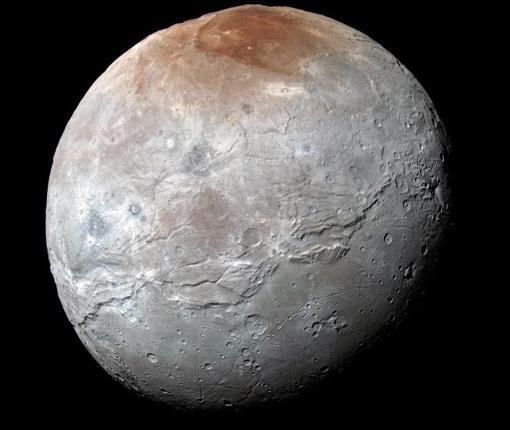 Vista en color mejorada de la luna más grande de Plutón, Caronte. Los colores están procesados para resaltar la variación de las propiedades de la superficie en la luna; lo más llamativo es la región polar norte (superior) rojiza.