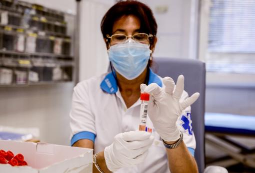 Una trabajadora sanitaria protegida sostiene una de las probetas utilizadas para la realización de PCR en Villaverde, Madrid, hoy