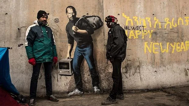 Dos hombres posan ante el grafiti de Steve Jobs realizado por Banksy en el campo de refugiados de Calais en diciembre pasado