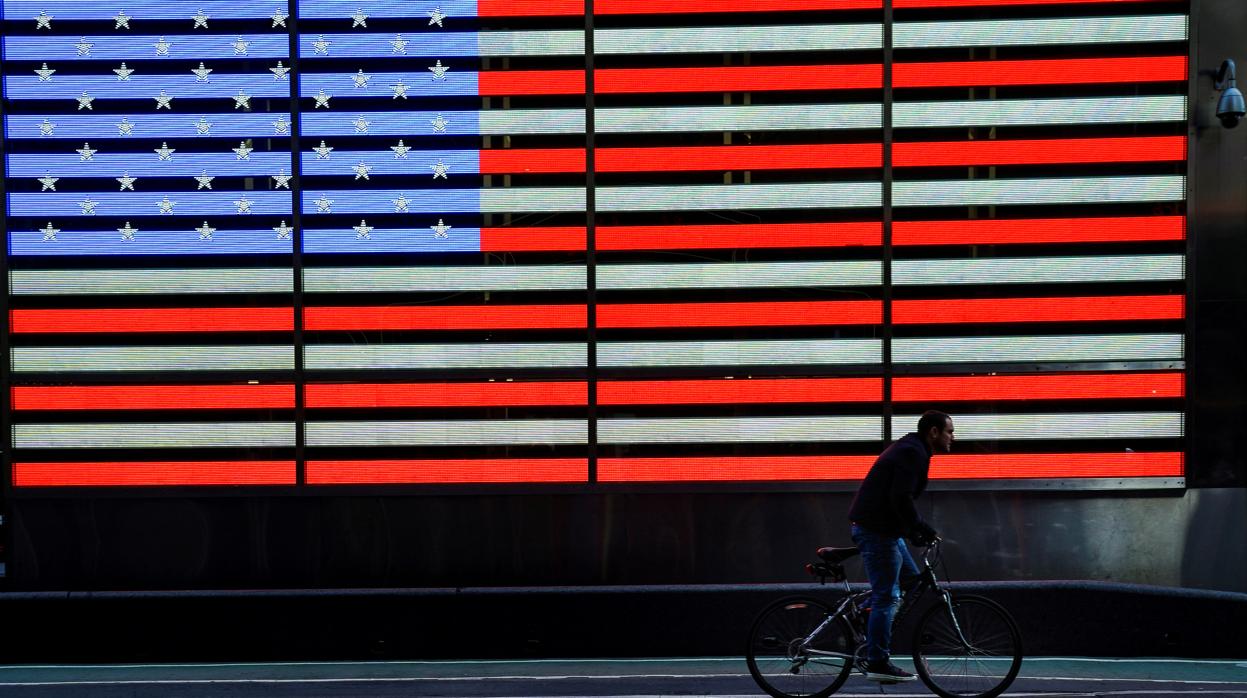 Un ciclista pasa ante un letrero luminoso con la bandera de Estados Unidos en Times Square, en Manhattan