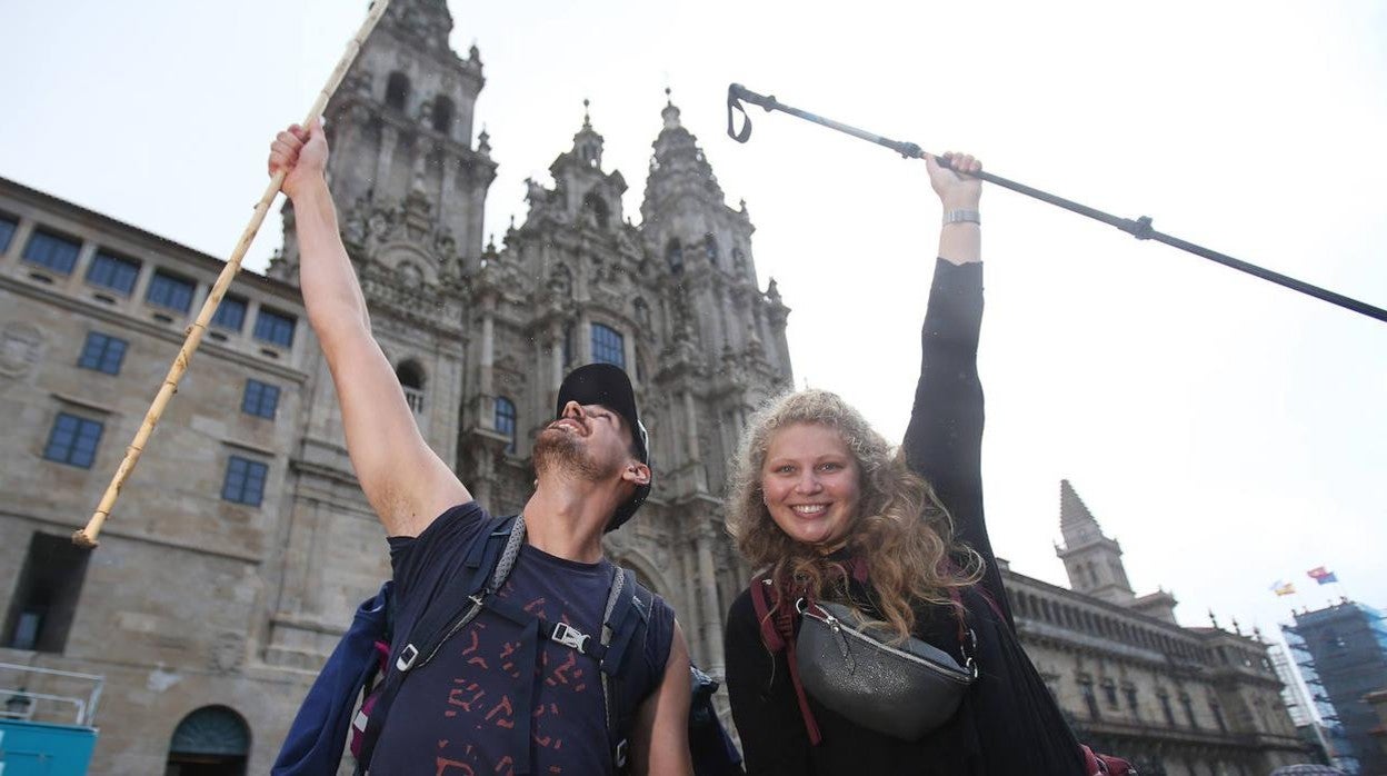 Dos peregrinos suben sus bastones al cielo tras llegar al final del Camino con la catedral de Santiago detrás