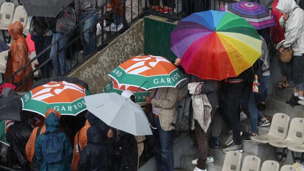 Varios aficionados se protegen de la lluvia en las pistas de Roland Garros