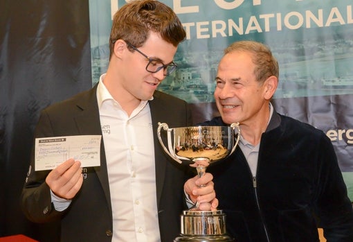 Magnus Carlsen sostiene su cheque y su trofeo tras ganar el torneo de la Isla de Man, patrocinado por Isai Scheinberg, que posa sonriente a su lado