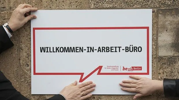 Dos empleados sostienen un cartel en el que se puede leer en alemán «Bienvenidos a la oficina de empleo»