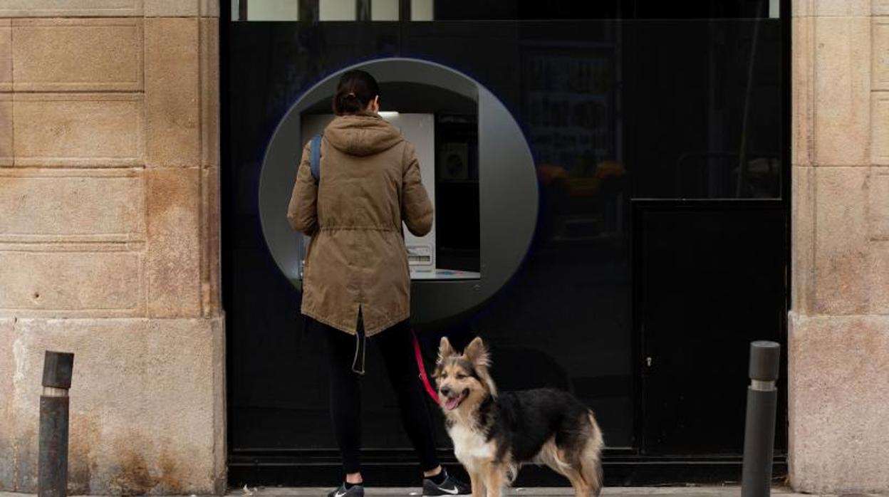 Una mujer saca dinero de un cajero y pasea a su perro en Barcelona