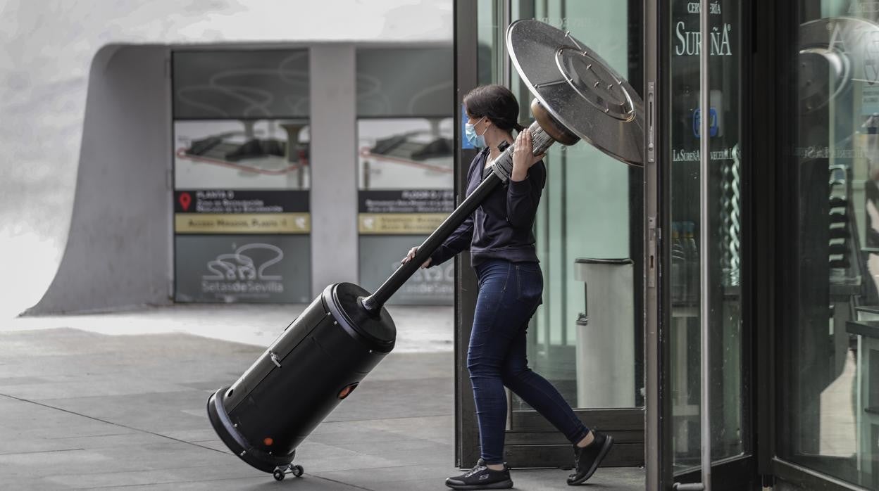 Una trabajadora de un establecimiento de hostelería retira una estufa de la terraza