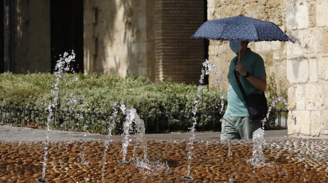 Un turista se protege del sol con un paraguas al lado de una surtidor de agua en Córdoba