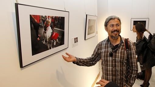 Uno de los fotógrafos participantes en la muestra posa junto a una imagen