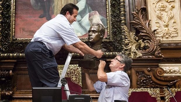 Dos operarios bajan el busto del Rey Juan Carlos de su lugar tradicional en el salón de plenos del Ayuntamiento de Barcelona