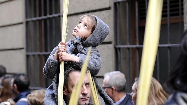 Una niña mira al cielo mientras sostiene una palma con sus manos