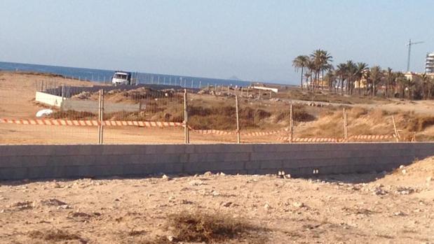 Muro de hormigón y valla metálica en construcción junto al palmeral y las dunas en Lo Ferrís