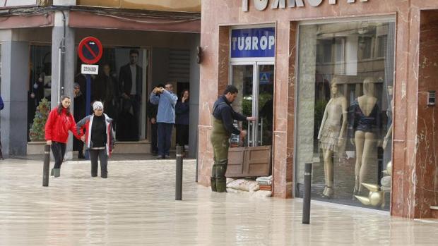 Varias personas se desplazan por una calle inundada por la lluvia en Orihuela, donde se han suspendido las clases