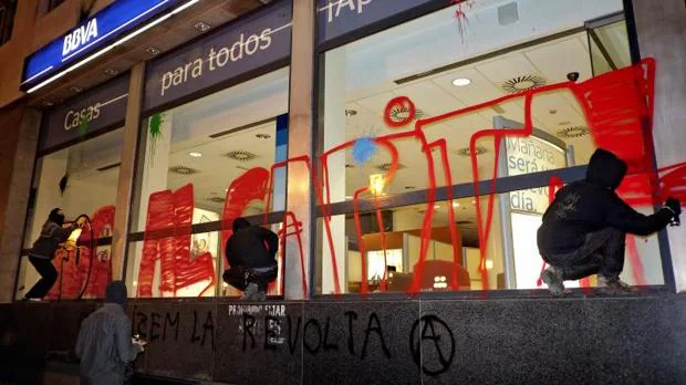 Grafiteros pintan el escaparate de una entidad bancaria en el centro de Valencia