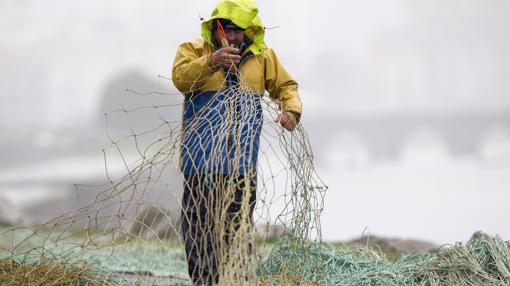 Un marinero cose las redes en Celeiro, cerca de Viveiro, bajo la intensa lluvia