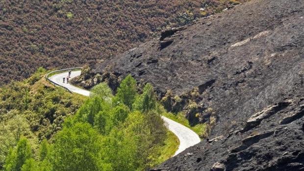 Unos ciclistas circulan junto a una ladera calcinada por un incendio forestal registrado en Quiroga (Lugo)