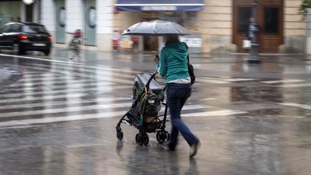 Una mujer con un carrito se protege con un paraguas de la lluvia caida esta tarde en el centro de la ciudad