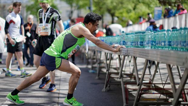 Un deportista hace ejercicios de estiramiento frente a una de las mesas de avituallamiento de agua para hidratación de los deportistas