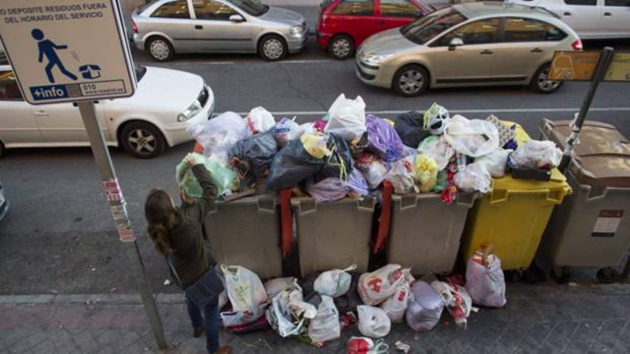 Una mujer tira la basura en un contenedor abarrotado de basura