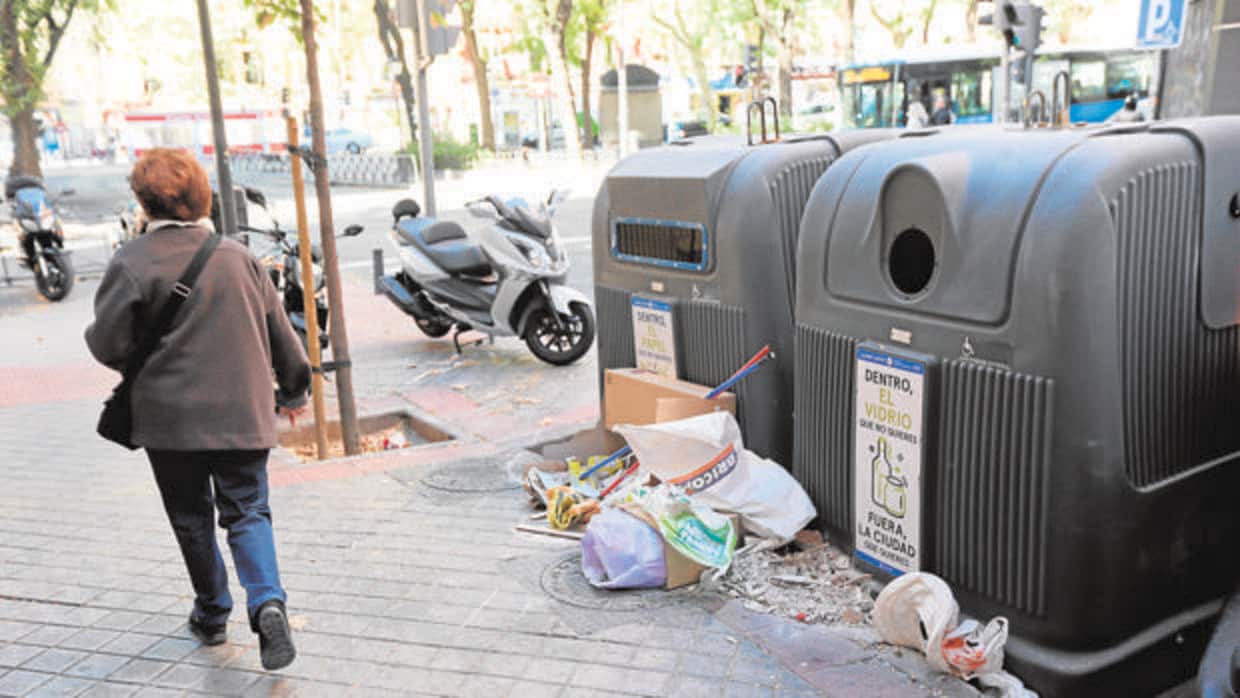Una mujer camina delante de un contenedor con residuos en Arganzuela